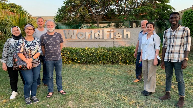 syv av menneskene som har vært med i prosjektet står oppstilt foran et "WorldFish"-skilt